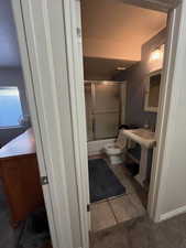 Bathroom with combined bath / shower with glass door and tile patterned floors