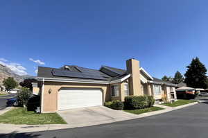 View of front facade with brick siding, a garage, roof mounted solar panels, a chimney, and concrete driveway