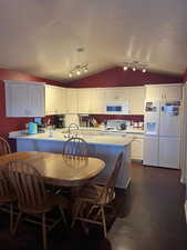 Kitchen featuring white appliances, vaulted ceiling, white cabinets, a peninsula, and light countertops