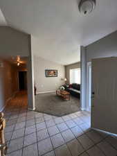 Living room with vaulted ceiling, light tile patterned floors, and light colored carpet