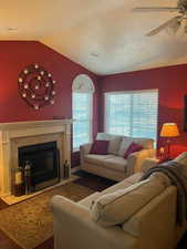 Living room featuring a ceiling fan, vaulted ceiling, a tiled fireplace, wood finished floors, and a textured ceiling