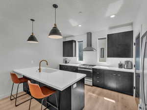 Kitchen featuring wall chimney range hood, appliances with stainless steel finishes, dark cabinets, light countertops, and decorative backsplash