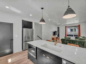 Kitchen with stainless steel appliances, dark cabinets, decorative light fixtures, light wood-type flooring, and recessed lighting