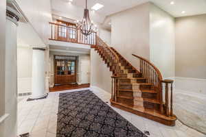 Tiled foyer entrance featuring a chandelier, stairway, recessed lighting, a towering ceiling, and ornate columns