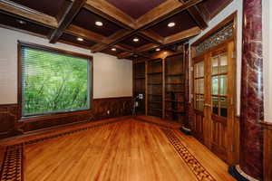 Unfurnished room featuring wood finished floors, coffered ceiling, wainscoting, beamed ceiling, and healthy amount of natural light
