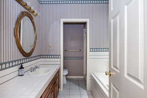 Bathroom with wallpapered walls, vanity, tiled tub, and tile patterned flooring