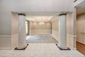 Entryway with ornate columns, ornamental molding, a raised ceiling, and a chandelier