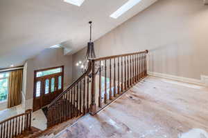 Stairway featuring a skylight, wood finished floors, a chandelier, and high vaulted ceiling