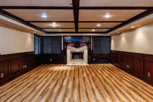 Cinema with a wainscoted wall, coffered ceiling, a fireplace, a decorative wall, and light wood finished floors