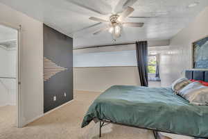 Carpeted bedroom with a walk in closet, a ceiling fan, and a textured ceiling