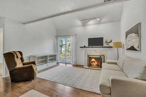 Living room featuring vaulted ceiling, a fireplace, wood finished floors.