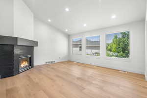 Unfurnished living room with a multi sided fireplace, light wood-style floors, recessed lighting, and vaulted ceiling