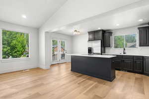 Kitchen with light countertops, a center island, decorative backsplash, lofted ceiling, and light wood finished floors