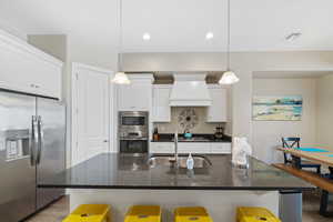 Kitchen with appliances with stainless steel finishes, custom exhaust hood, a breakfast bar, white cabinets, and recessed lighting