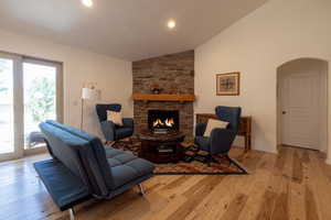 Living room with vaulted ceiling, arched walkways, light wood-type flooring, a stone fireplace, and recessed lighting