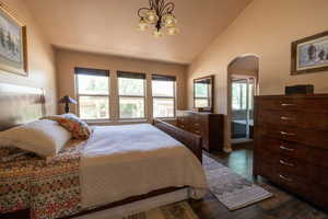 Bedroom featuring arched walkways, a chandelier, lofted ceiling, and dark wood-style floors