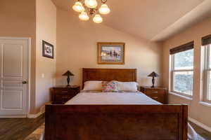 Bedroom with a chandelier, dark wood-style flooring, and vaulted ceiling