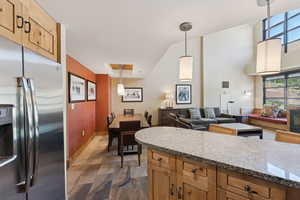Kitchen with stainless steel refrigerator with ice dispenser, pendant lighting, open floor plan, light stone countertops, and brown cabinets