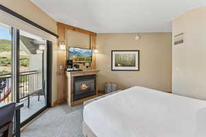 Bedroom with access to outside, a glass covered fireplace, and light carpet
