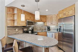 Kitchen featuring appliances with stainless steel finishes, a peninsula, open shelves, light brown cabinets, and tasteful backsplash