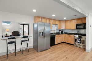 Kitchen with black and stainless-steel appliances, light wood-style floors, light brown cabinetry, decorative backsplash, and recessed lighting