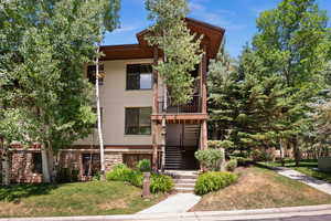 View of front of house with stucco siding, a front lawn, stone siding, and stairs