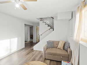 Living area with stairway, wood finished floors, and a ceiling fan