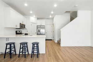 Kitchen featuring stainless steel appliances, light wood-type flooring, a peninsula, a kitchen bar, and recessed lighting