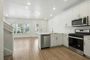 Kitchen with appliances with stainless steel finishes, light wood-style flooring, a peninsula, recessed lighting, and white cabinetry
