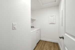 Laundry area with electric panel, independent washer and dryer, light wood finished floors, and attic access