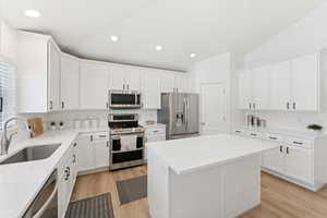 Kitchen featuring appliances with stainless steel finishes, lofted ceiling, light wood-style flooring, a center island, and white cabinetry