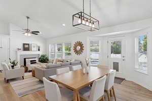 Dining area with light wood-style floors, vaulted ceiling, a tiled fireplace, ceiling fan, and recessed lighting