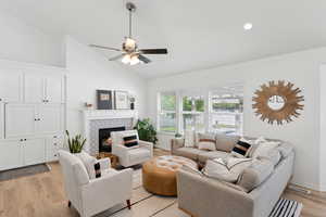 Living room featuring light wood finished floors, ceiling fan, a fireplace, high vaulted ceiling, and recessed lighting