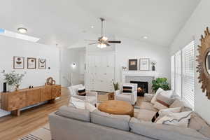 Living room with vaulted ceiling, a tiled fireplace, a ceiling fan, light wood-style floors, and recessed lighting