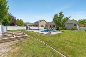 View of pool with a water slide, a fenced backyard, a patio, and a garden
