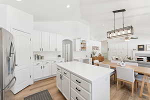 Kitchen featuring stainless steel refrigerator with ice dispenser, ceiling fan, arched walkways, white cabinets, and a kitchen island