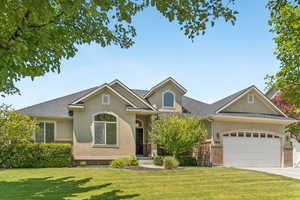 View of front of property with brick siding, stucco siding, a front yard, and an attached garage