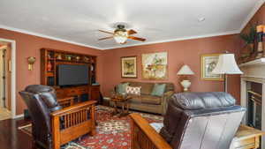 Living room with ceiling fan, wood finished floors, crown molding, and a glass covered fireplace