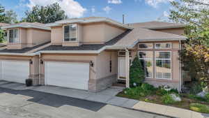 View of front of property with an attached garage, stucco siding, brick siding, a shingled roof, and driveway