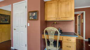 Office space with built in desk, dark wood-style floors, and ornamental molding