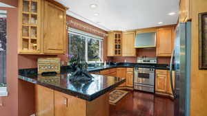 Kitchen with appliances with stainless steel finishes, wall chimney exhaust hood, a peninsula, recessed lighting, and dark wood-style flooring