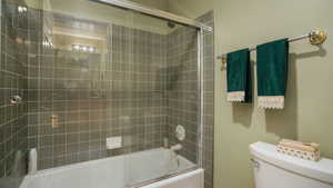 Full bathroom with toilet and bath / shower combo with glass door