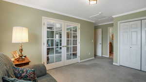 Living area with french doors, attic access, carpet, and ornamental molding