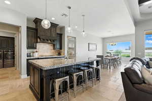 Kitchen featuring open floor plan, backsplash, dark brown cabinets, recessed lighting, and a breakfast bar area