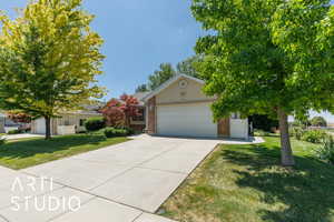 View of property hidden behind natural elements featuring a garage, a front lawn, concrete driveway, and brick siding