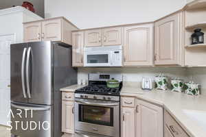 Kitchen featuring appliances with stainless steel finishes, light brown cabinetry, and open shelves