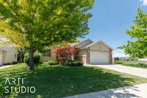 View of property hidden behind natural elements featuring an attached garage, driveway, a front yard, and brick siding