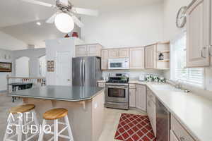 Kitchen featuring appliances with stainless steel finishes, a breakfast bar area, a center island, ceiling fan, and high vaulted ceiling