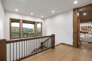 Corridor with an upstairs landing, wood-type flooring, and recessed lighting