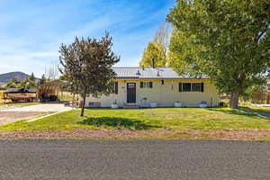 Ranch-style home with a front yard, a detached carport, a metal roof, driveway, and entry steps